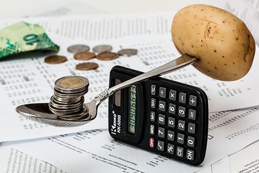  a spoon placed on top of a vertical calculator balancing between stack of coins and a potato depicting the management of expenses in a financial statement