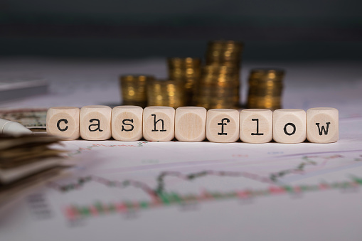 the word cashflow of financial statement spelled on wooden blocks with a stack of coins in the background